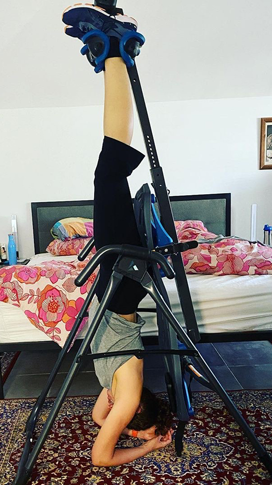 Teeter FitSpine Happy Back Club - person hanging upside down on inversion table in bedroom